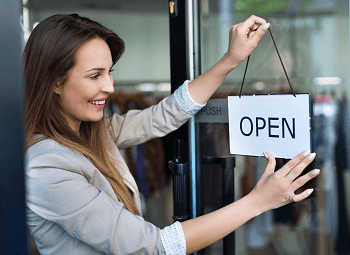 woman small business owner puts an open sign up on door to her store