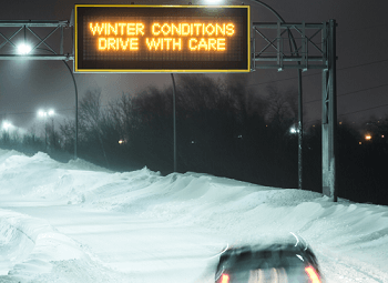 car driving down a freeway heavily covered in snow overhead sign reads winter conditions drive with care